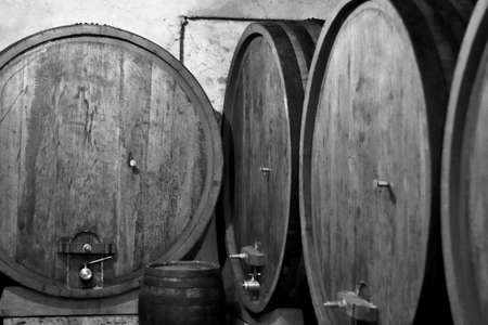 wooden barrels stacked for the production, storage and aging of Italian wine, in a dark and cool...
