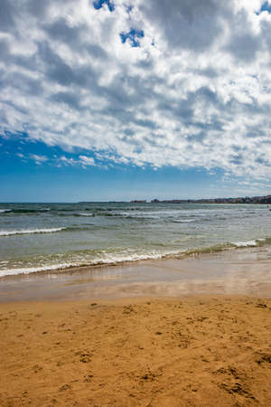 Nettuno, Lazio, Rome, Italy. Some people walk, play and relax on the shore, on the beach of the Roman sea. Backlit. Reflections of light on the water. Cloudy blue sky at sunset. Houses of the city.の写真素材