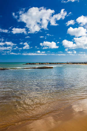 Nettuno, Lazio, Rome, Italy. Some people walk, play and relax on the shore, on the beach of the Roman sea. Backlit. Reflections of light on the water. Cloudy blue sky at sunset. Houses of the city.の写真素材