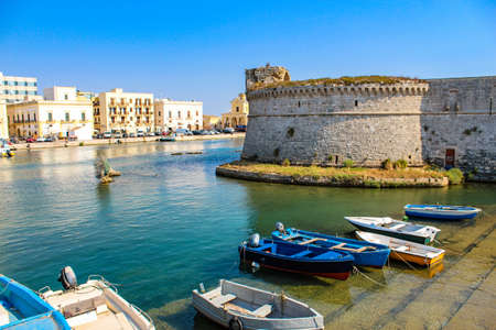 The castle fortress overlooking the sea, in the town of Gallipoli, in Puglia, Italy. The boats moored. The blue sky.のeditorial素材