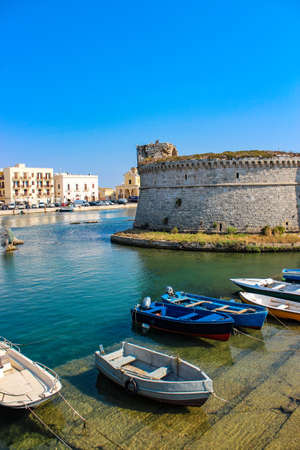 The castle fortress overlooking the sea, in the town of Gallipoli, in Puglia, Italy. The boats moored. The blue sky.のeditorial素材