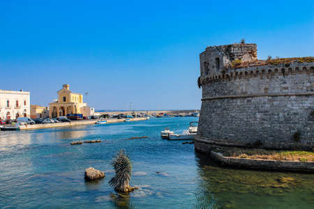 The castle fortress overlooking the sea, in the town of Gallipoli, in Puglia, Italy. The boats moored. The blue sky.のeditorial素材