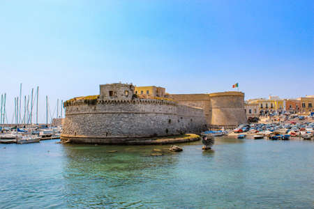 The castle fortress overlooking the sea, in the town of Gallipoli, in Puglia, Italy. The boats moored. The blue sky.のeditorial素材