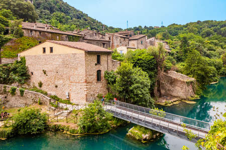 A glimpse of the small village of Stifone, on the Nera river. Umbria, Terni, Italy. The walls of stones and bricks. The bridge over the river with clear blue waters. Tourists stroll through the alleysの写真素材