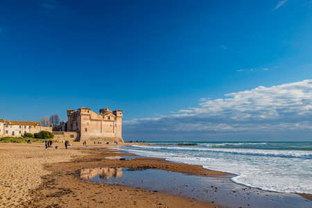Santa Marinella, Rome, Lazio, Italy - Sea shore of the Roman coast of Santa Severa on a winter day. Many people stroll and enjoy the sun on the beach, at sunset. Rough sea, wind, cloudy blue skyの写真素材