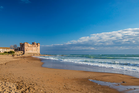 Santa Marinella, Rome, Lazio, Italy - Sea shore of the Roman coast of Santa Severa on a winter day. Many people stroll and enjoy the sun on the beach, at sunset. Rough sea, wind, cloudy blue skyの写真素材
