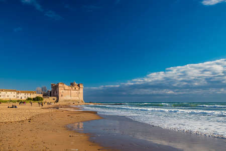 Santa Marinella, Rome, Lazio, Italy - Sea shore of the Roman coast of Santa Severa on a winter day. Many people stroll and enjoy the sun on the beach, at sunset. Rough sea, wind, cloudy blue skyの写真素材