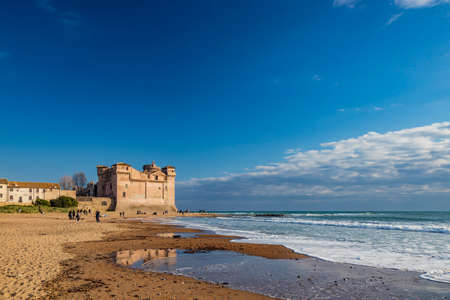 Santa Marinella, Rome, Lazio, Italy - Sea shore of the Roman coast of Santa Severa on a winter day. Many people stroll and enjoy the sun on the beach, at sunset. Rough sea, wind, cloudy blue skyの写真素材