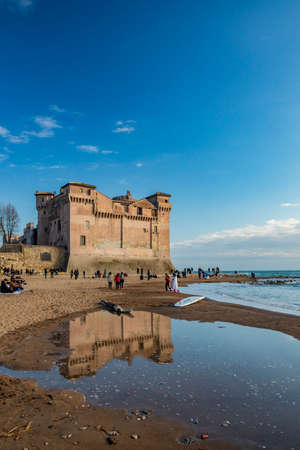 March 14, 2022 - Santa Marinella, Rome, Lazio, Italy - The seaside castle of Santa Severa on a winter day. The rough sea, wind, the cloudy blue sky. Many people stroll and enjoy the sun on the beach.のeditorial素材