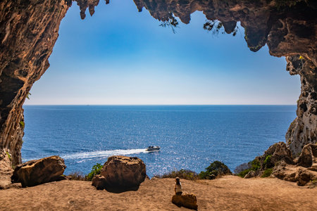 Gagliano del Capo. The spectacular Cipolliane caves, on the rocky cliff of Salento. A little girl admires the amazing panorama of the blue sea and a speedboat goes by. The entrance to the cave.の写真素材