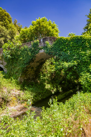 The small medieval village of Corchiano, in the province of Viterbo, in Lazio. The ancient Roman bridge over the Rio Fratta, in the gorge park, partly covered by vegetation.の写真素材