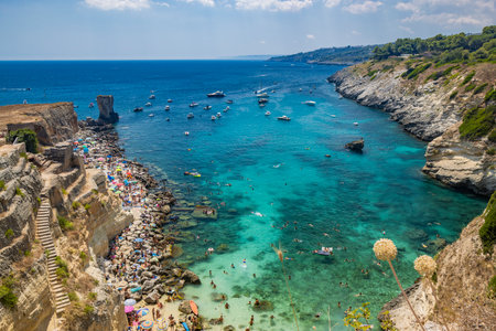 The amazing bay of Porto Miggiano, in Santa Cesarea Terme, resort of Salento, Puglia, Italy. Full of tourists and boats, in the clear, blue and turquoise sea. Small beach enclosed between high cliffsの写真素材