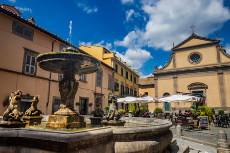 July 2, 2023 - Tuscania, Viterbo, Lazio. A glimpse of the ancient medieval village of Tuscania, city of the Etruscans. The square with the church and the large fountain.のeditorial素材