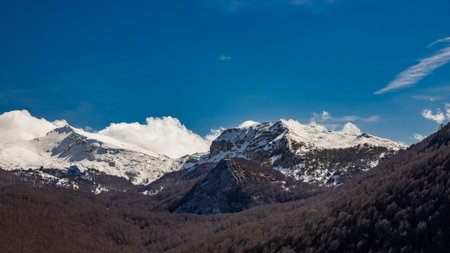 The snow-capped mountains of the Abruzzo Apennines, in Campo Felice, Italy. Below, a beech forest, with bare trees in winter. The white clouds on the rocky mountain peaks.の写真素材