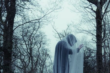 A ghostly hooded figure standing in a forest in winter. 