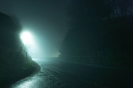 A spooky, eerie country road passing through a hill. On a mysterious foggy, winters night.の写真素材
