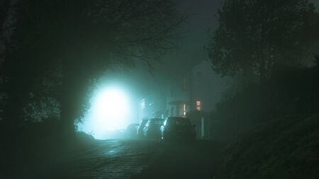 Houses with lights glowing from windows, on a road in the countryside, on a spooky atmospheric moody foggy winters nightの写真素材