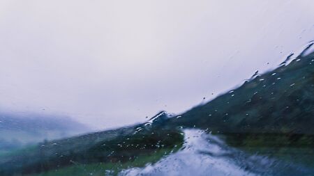Looking out of a car windscreeen as rain comes down. With an out of focus gloomy road and...