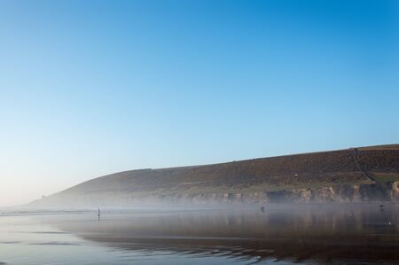 Surfers on the beach silhouetted in the afternoon sun on a warm February day. Saunton, Devon, 27th Feb 2019.の写真素材