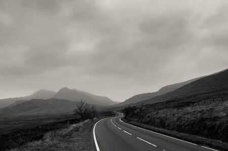 An atmospheric black and white edit of a road heading towards mountains on a stormy winters day. Snowdonia, Wales. UK.の写真素材