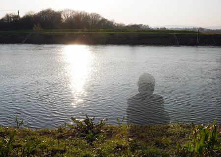 A transparent hooded figure sitting next to a river on a sunny afternoon.                の写真素材