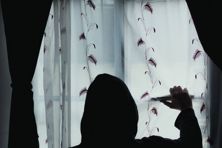 Signifying mental health and isolation  concept. A hooded figure, looking out of a window.