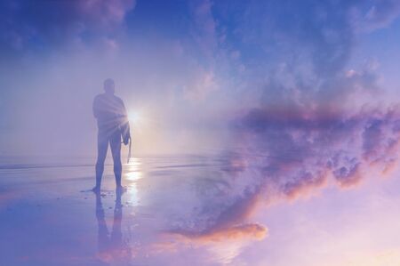 Silhouette of a surfer on a beach looking at the sunset. With a double exposure of the sky and an abstract, experimental dream like edit.の写真素材