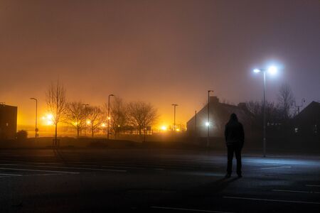 A hooded figure standing in an empty industrial estate on a misty winters night.の写真素材