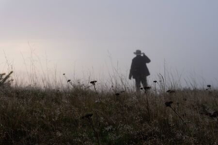 A mysterious figure standing out of focus in a field in the background. With a close up of plants on a misty winters dayの写真素材