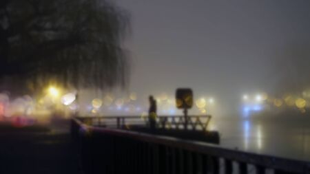 A mysterious figure standing by street lights next to a river on a misty winters night. With a blurred, bokeh, out of focus edit              の写真素材