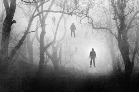 A spooky, eerie forest in winter, With a men floating against a bright light, with the trees silhouetted by fog. With a grunge, vintage, textured editの写真素材