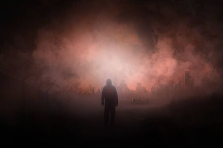 A post apocalypse scene showing a man standing in a ruined city looking at a destroyed city. With smoke covering the sky.の写真素材