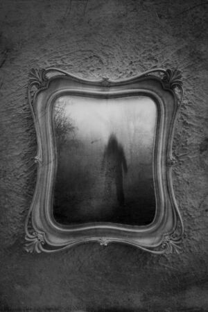Horror concept of a ghostly figure in a mirror. With a grunge, blurred, textured, black and white edit.の写真素材