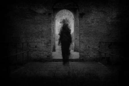 A spooky ghost, walking towards the camera, framed by the archway of an old building. With a grunge, vintage, blurred edit.の写真素材