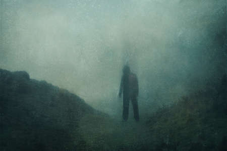 A ghostly blurred hooded figure. standing in a valley on a foggy evening. With a grunge, textured...