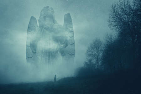 A ghostly giant statue of a graveyard angel in the countryside. On an atmospheric foggy winters night.の写真素材