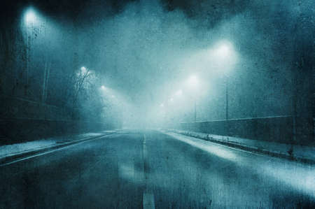 A moody concept of a straight road with street lights on a foggy winters night. With a grunge,...