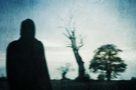 A man looking at a tree in a field on a spooky winters day in the countryside. With a grunge,...