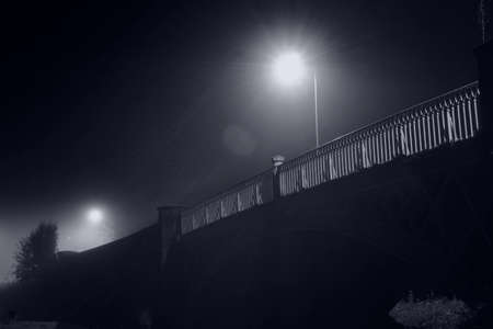 Looking up at the railings on a bridge. Illuminated by street lights. On a atmospheric foggy night.の写真素材