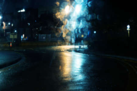 A wet city road at night lit by street lights. Shot through a car window, creating a bokeh reflection effect.の写真素材