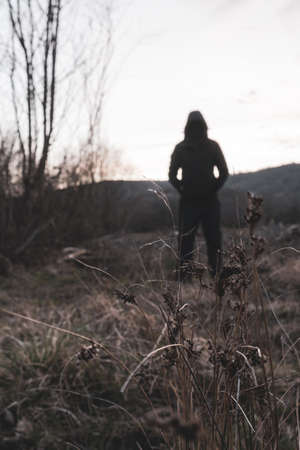 A blurred out of focus edit. A moody hooded figure, standing in the countryside looking at the evening sky. With a vertical profile.の写真素材