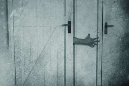 A horror concept of a spooky arm coming out of an old wooden door in a house. With a grunge, textured editの写真素材
