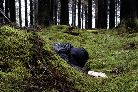 A murder, crime concept of a hooded man, face down in a dark forest on a bleak, wet day