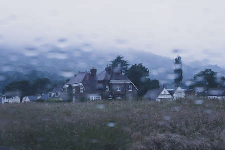 Looking out onto an historic home across a field. As raindrops blur a car window. On a moody summers evening. UKの写真素材