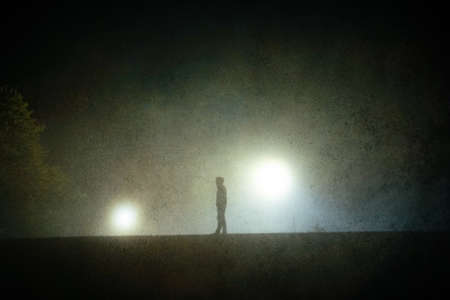 A spooky hooded figure, silhouetted against street lights at night. With a grunge, artistic edit.