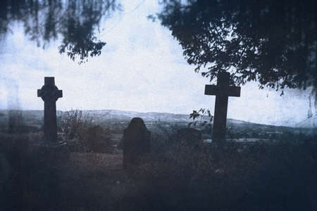 A spooky graveyard with crosses silhouetted against the sky in the countryside. With a grunge, vintage edit.の写真素材