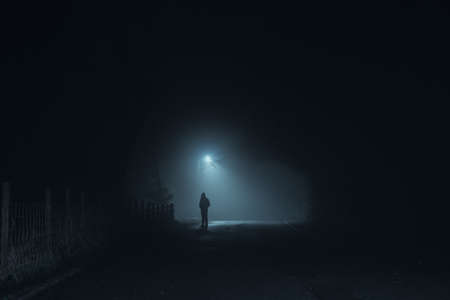 A dark scary concept of a man silhouetted against a street light on a spooky, foggy winters nightの写真素材