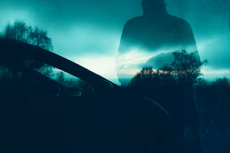 A missing person, ghost concept. Of a transparent man standing next to a car on a spooky winters evening. With a grunge, blurred editの写真素材