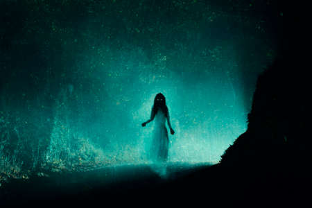 A supernatural concept of a spooky ghost woman, haunting a country road on a foggy winters night. With a grunge, vintage edit.の写真素材