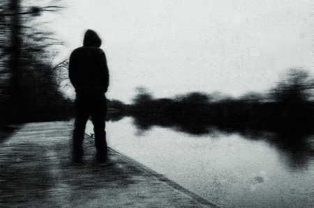 A spooky mysterious hooded figure looking at a river. On a bleak winters day. With an abstract, grunge, blurred edit.の写真素材